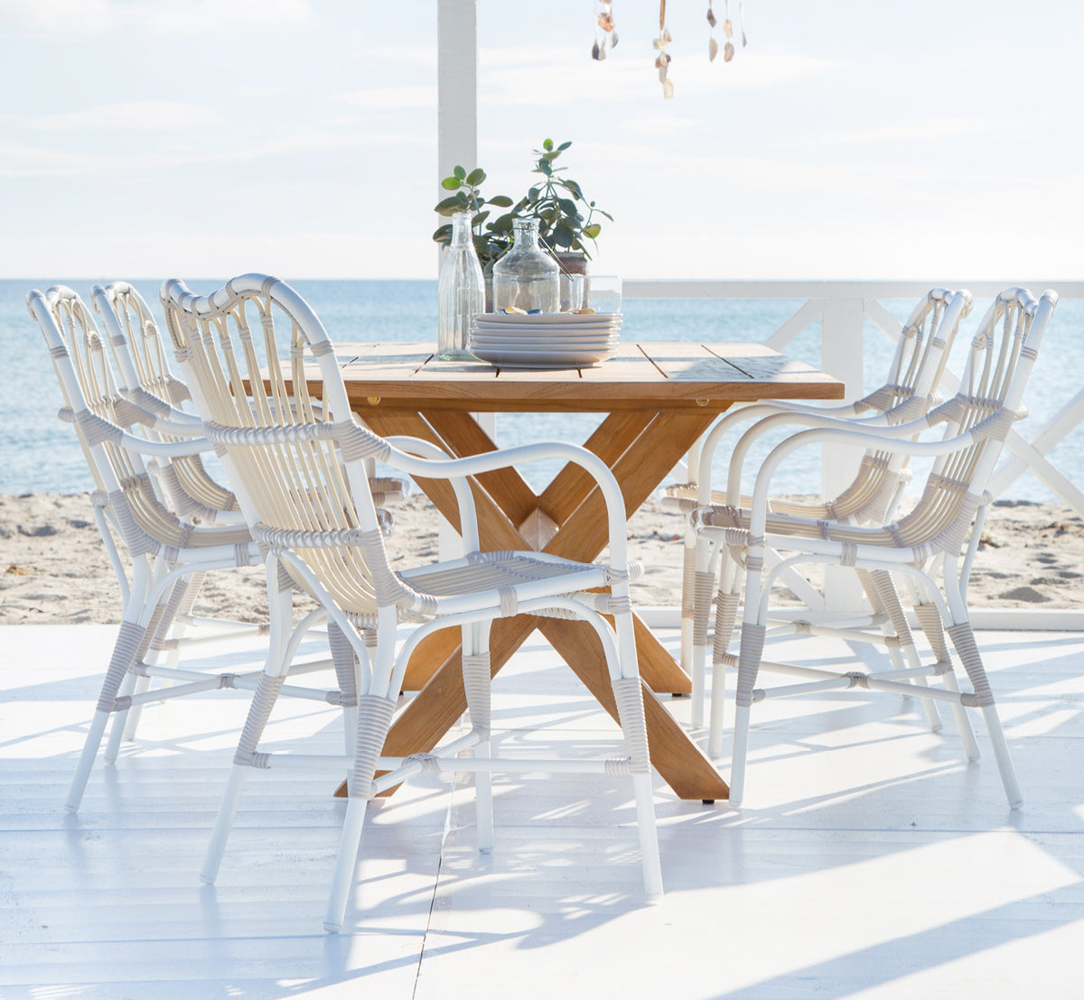 Esta es una imagen de estilo de vida de Colonial mesa 160 en outdoor Teak, en una terraza junto a la playa con cubierta de madera blanca y vistas al.