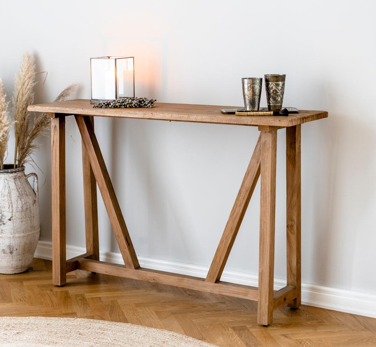 Esta es una imagen de estilo de vida de Lucas Teak consola en teak indoor. Estilizada con portavelas y hierba de las pampas en un ambiente cálido con alfombra de yute.
