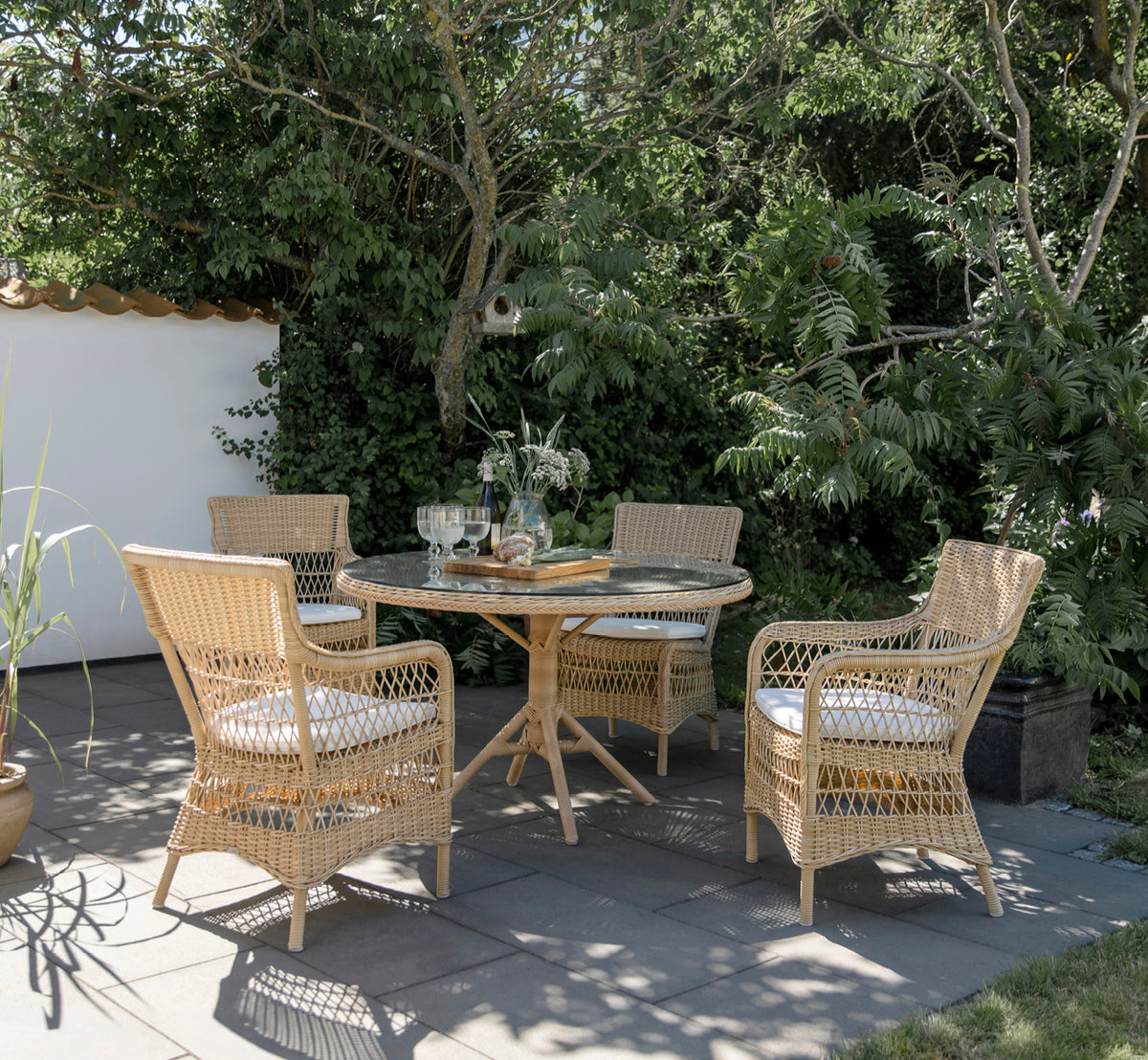 Esta es una imagen de estilo de vida de Grace mesa de comedor exterior en natural ArtFibre Aluminium, en un exuberante patio de jardín con suelo de.