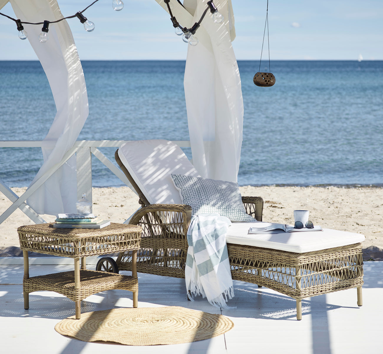 Esta es una imagen de estilo de vida de Susy mesa auxiliar en antique Grey ArtFibre Aluminium, en una terraza costera con vistas al mar, gramíneas de.