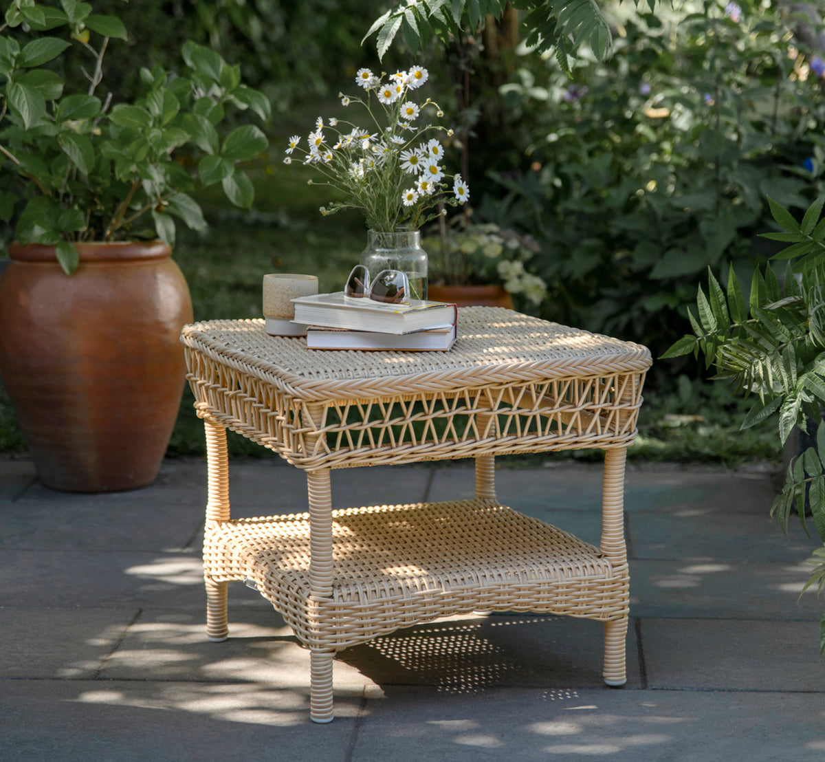 Esta es una imagen de estilo de vida de Susy mesa auxiliar en natural ArtFibre Aluminium, en una terraza costera con vistas al mar, gramíneas de.