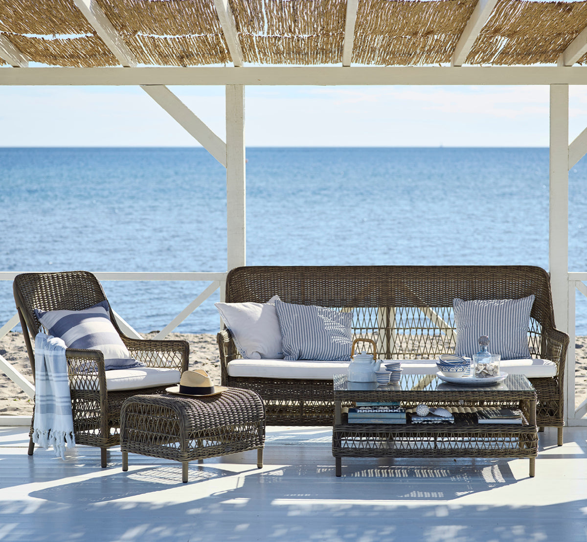 Esta es una imagen de estilo de vida de Hazel mesa de centro en antique Grey ArtFibre Aluminium, en una terraza costera sombreada con dosel de caña y.