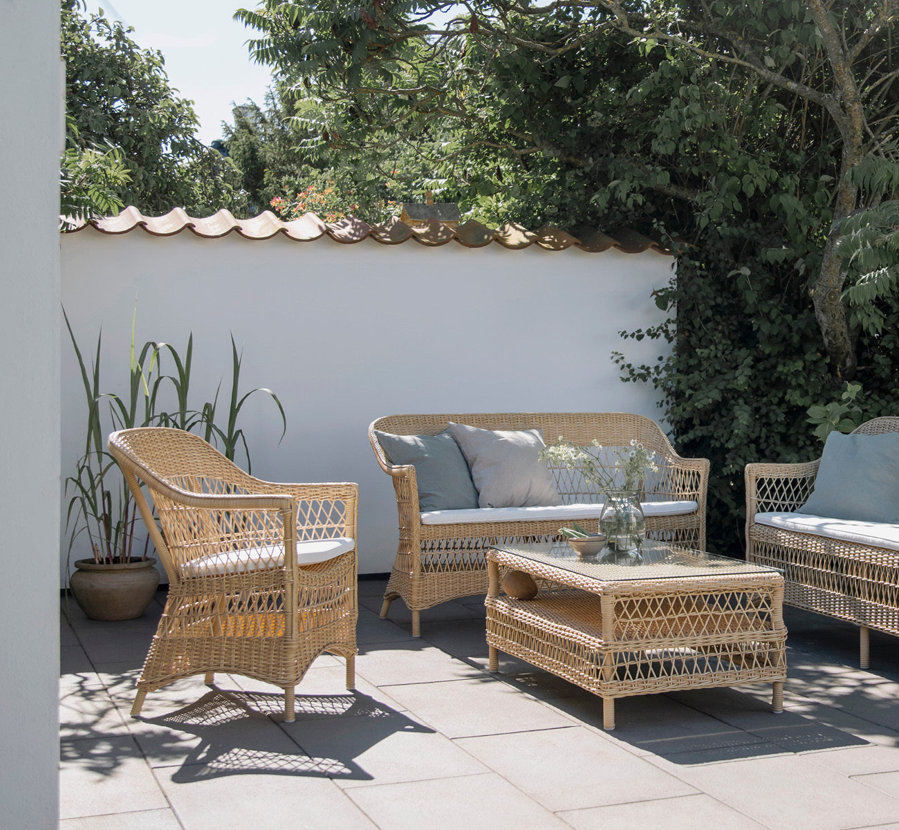 Esta es una imagen de estilo de vida de Hazel mesa de centro en natural ArtFibre Aluminium, en una terraza costera sombreada con dosel de caña y.