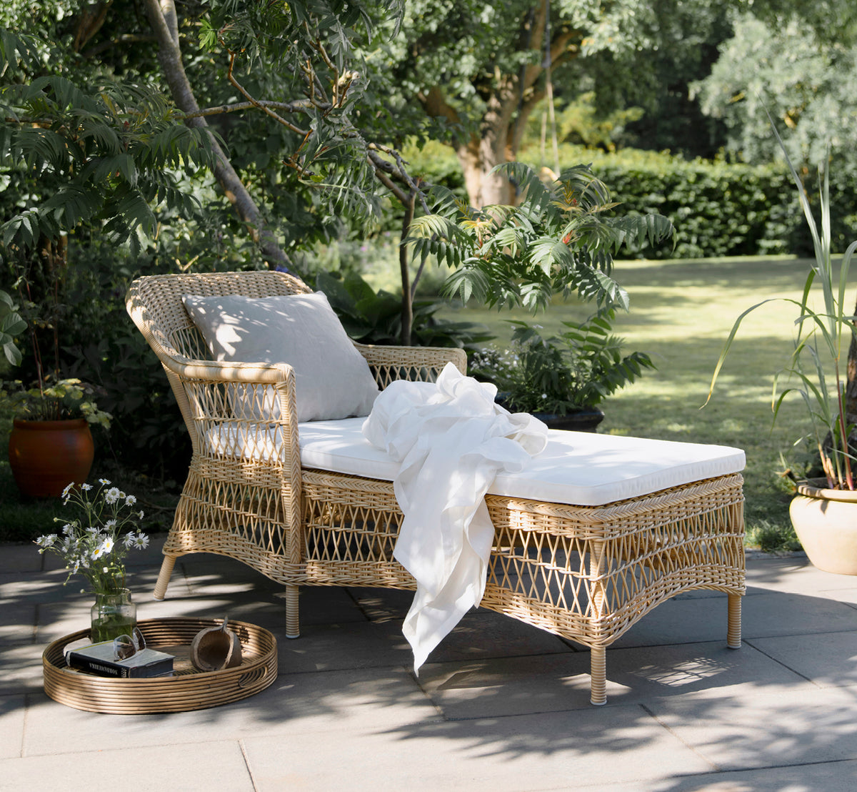 Esta es una imagen de estilo de vida de Olivia Exterior Sunbed i natural artfibre aluminium. En un entorno de jardín con manta blanca y almohada.