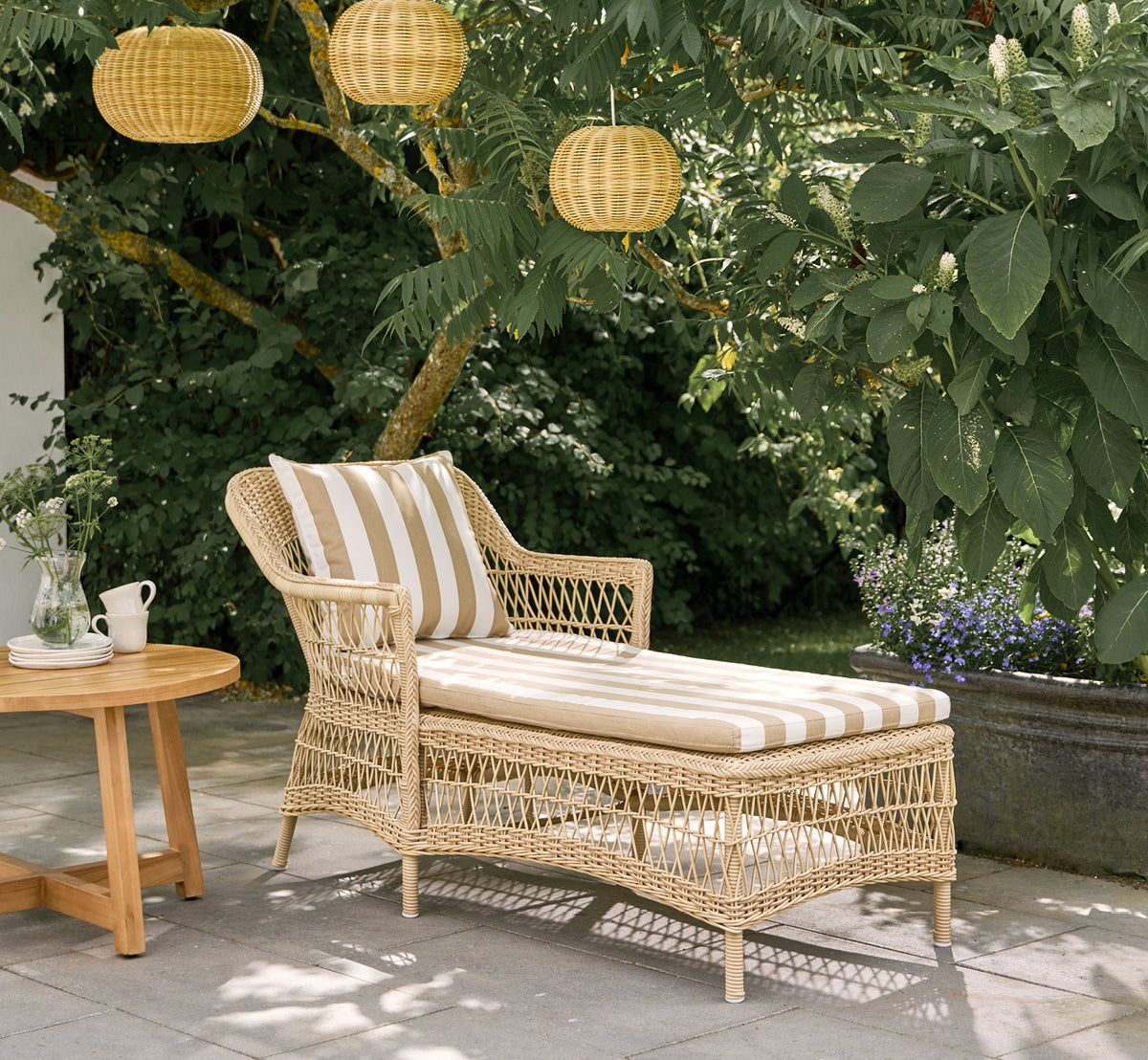 Esta es una imagen de estilo de vida de Olivia Exterior Sunbed i natural artfibre aluminium. En un patio con cojín a rayas y faroles.