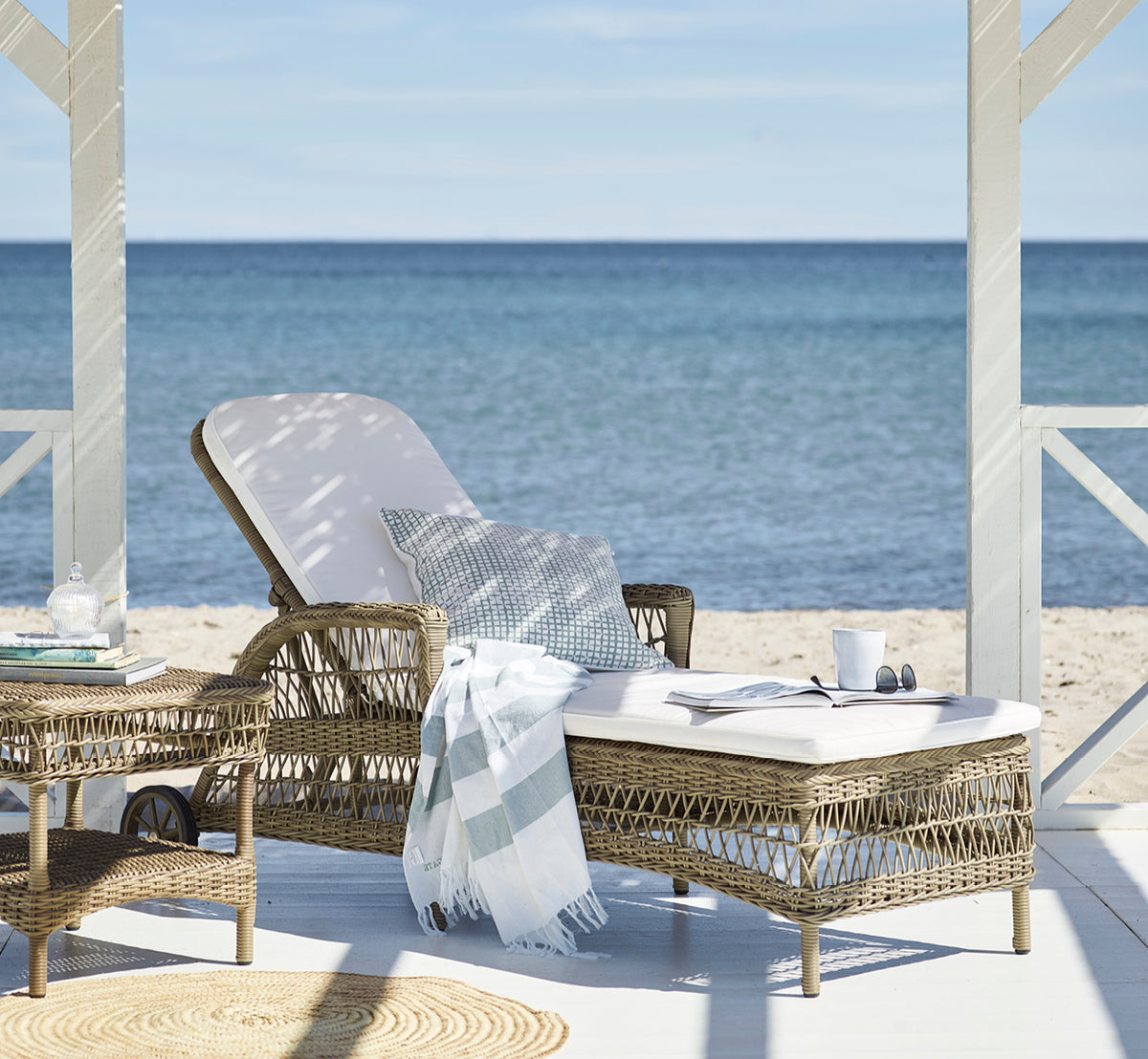 Esta es una imagen de estilo de vida de Daisy tumbona en antique Grey ArtFibre Aluminium, en una terraza de jardín rodeada de frondosos árboles y.