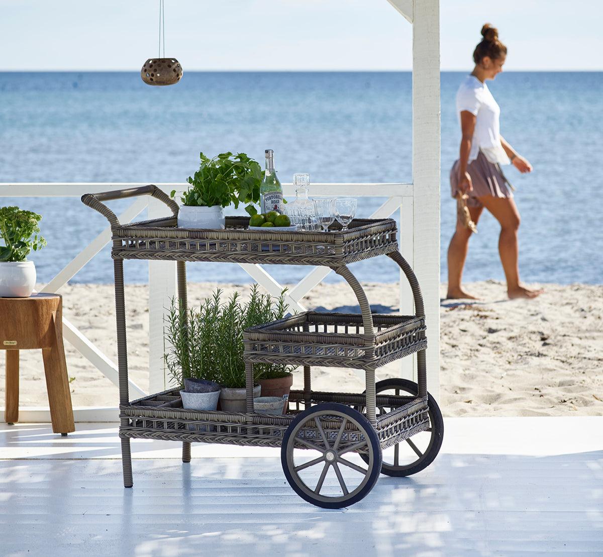 Esta es una imagen de estilo de vida de James carrito en antique grey artfibre aluminium, en una terraza de playa bajo una pérgola blanca con vistas.