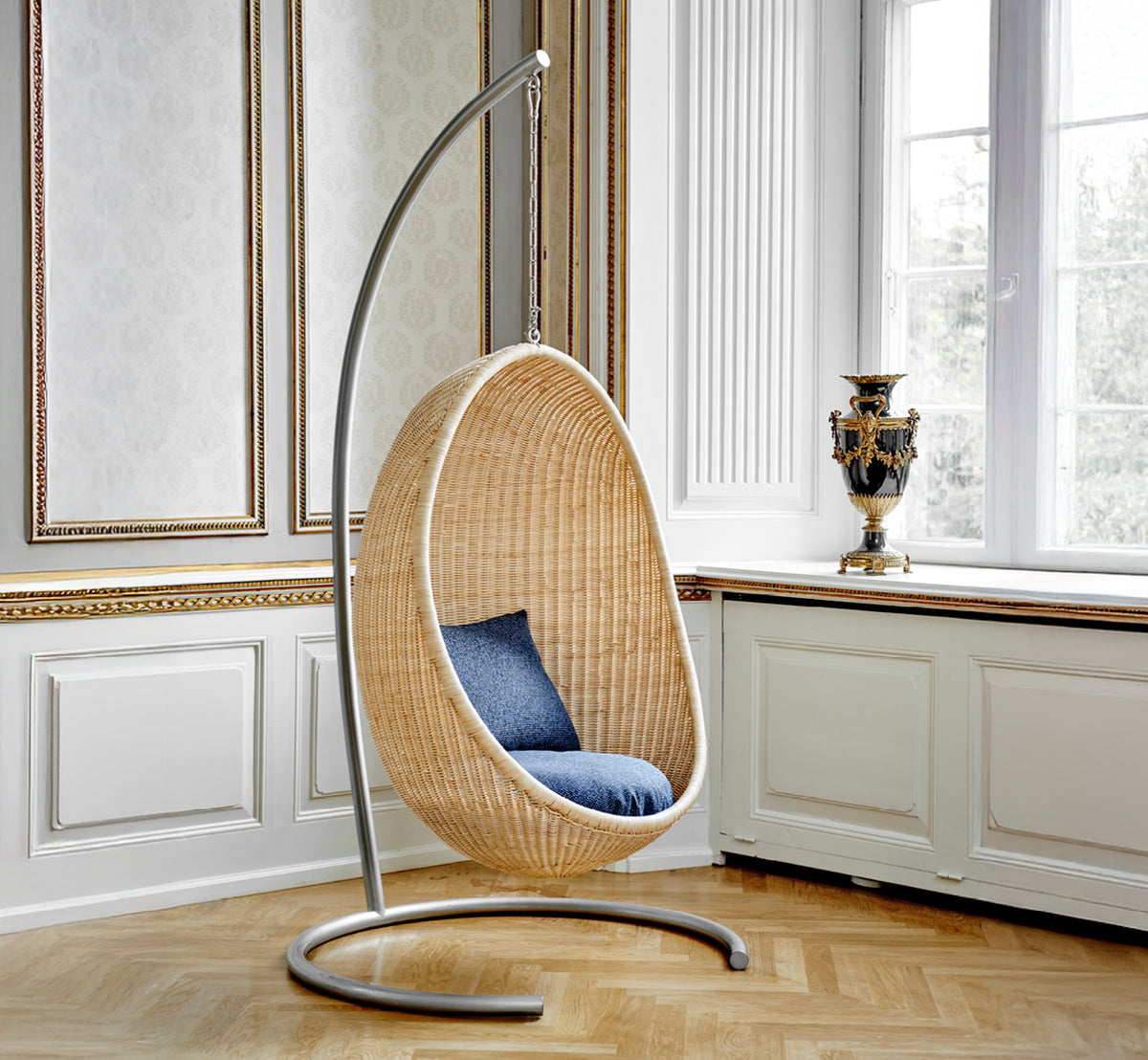 Esta es una imagen de estilo de vida de Stand silla colgante en metal stand, en un elegante interior clásico con elaboradas molduras doradas.