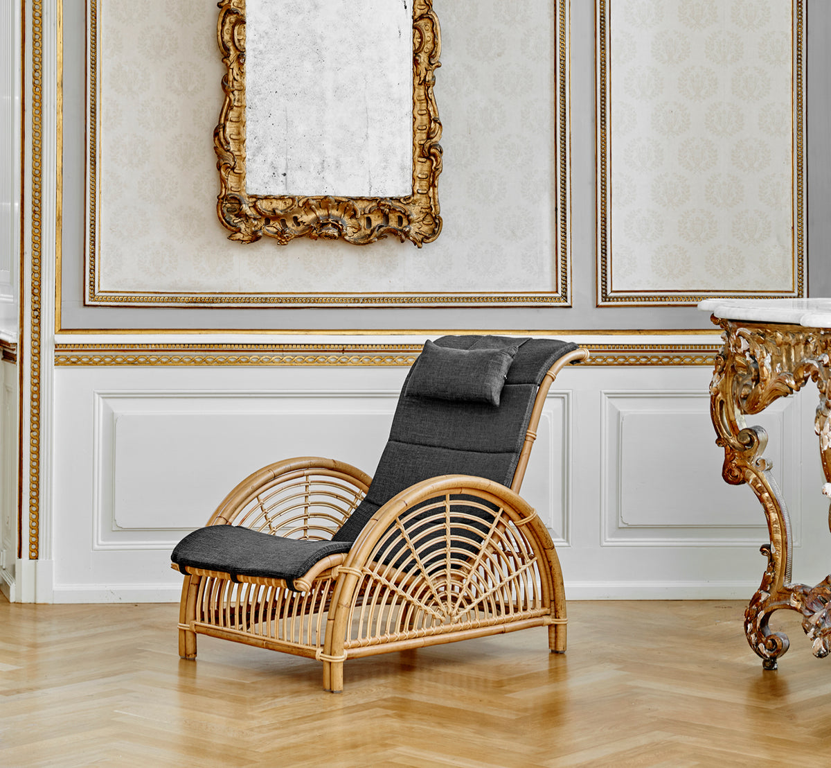 Esta es una imagen de estilo de vida de Paris sillón lounge en polished natural rattan. Colocada sobre un suelo de parqué en espiga junto a un banco a juego.