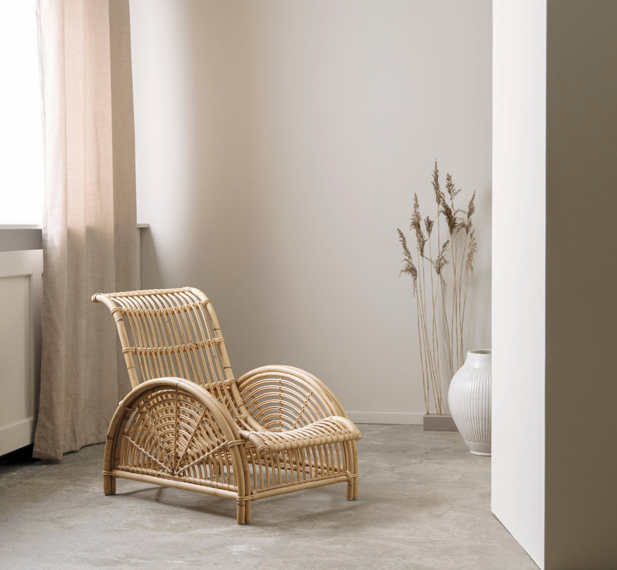 Esta es una imagen de estilo de vida de Paris sillón lounge en polished natural rattan. Colocada sobre un suelo de parqué en espiga junto a un banco a juego.