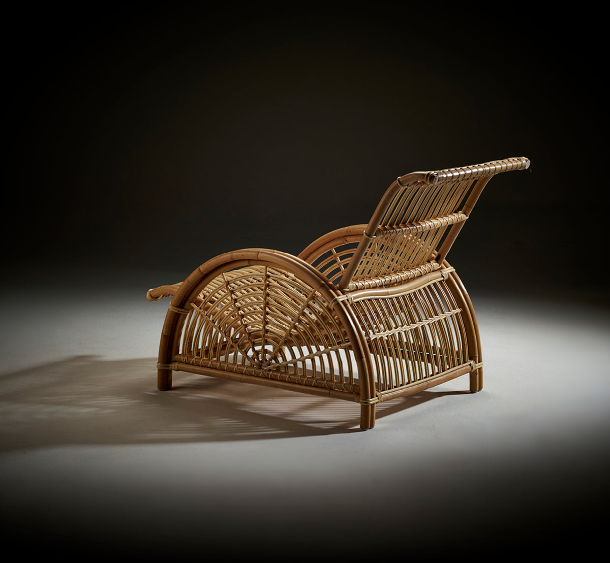 Esta es una imagen de estilo de vida de Paris sillón lounge en polished natural rattan. Colocada sobre un suelo de parqué en espiga junto a un banco a juego.
