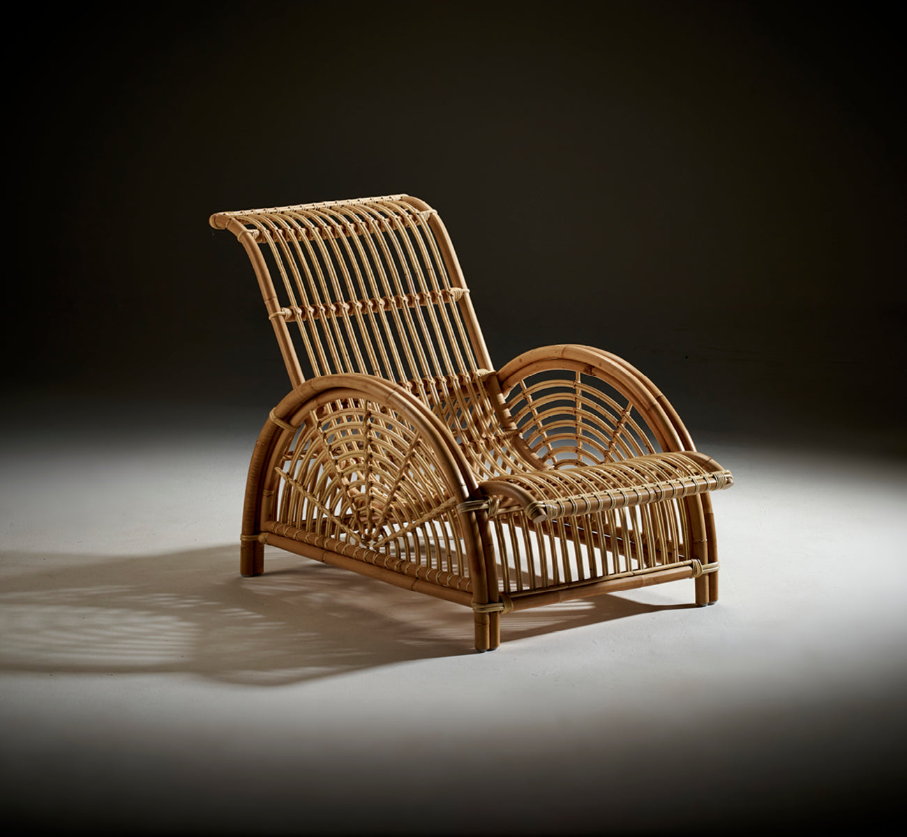 Esta es una imagen de estilo de vida de Paris sillón lounge en polished natural rattan. Colocada sobre un suelo de parqué en espiga junto a un banco a juego.