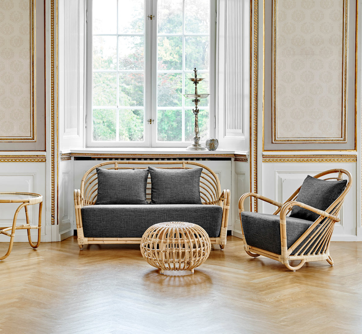 Esta es una imagen de estilo de vida de Charlottenborg sofá en polished Natural Rattan, en un elegante interior clásico con elaboradas molduras.
