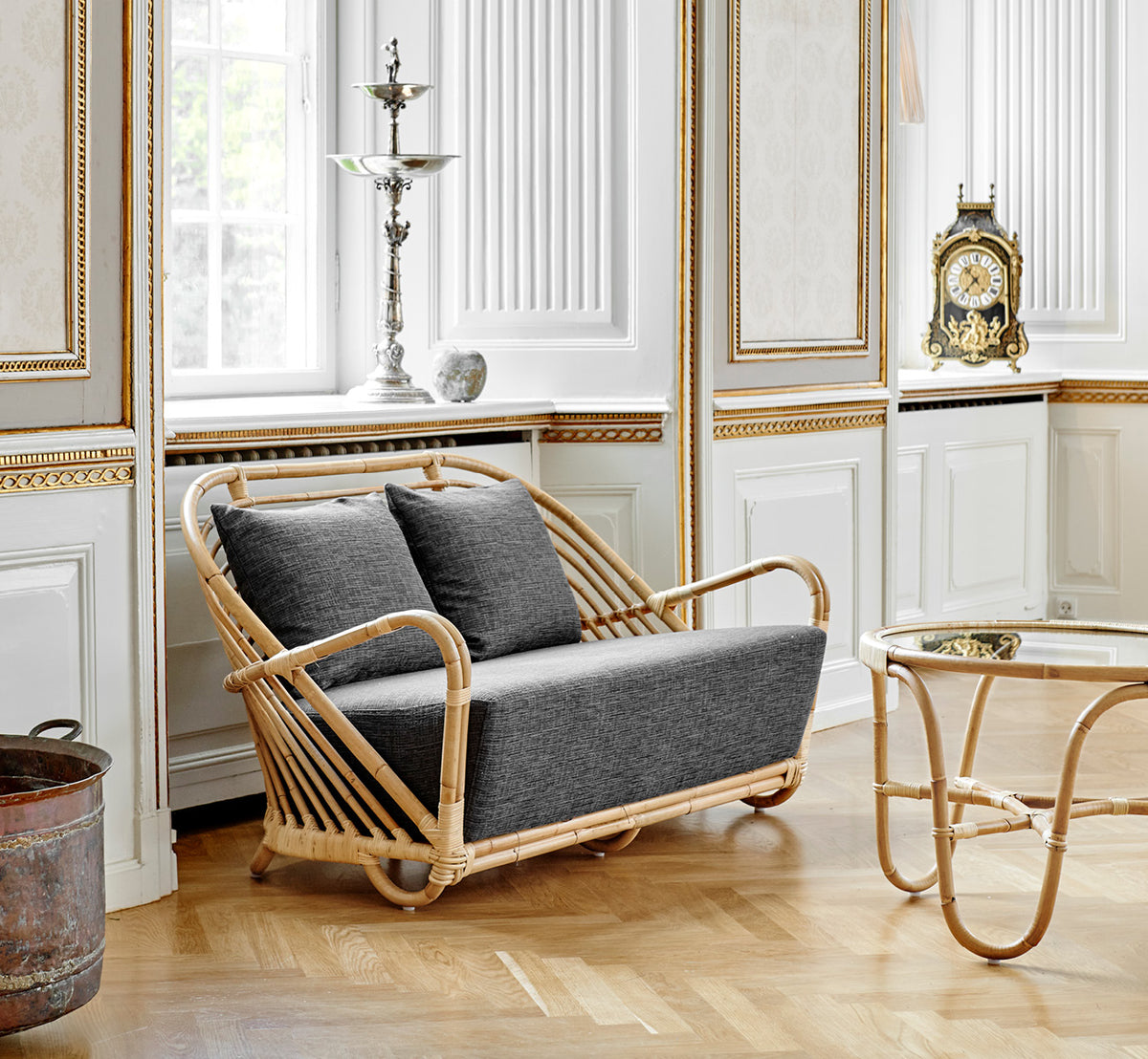 Esta es una imagen de estilo de vida de Charlottenborg sofá en polished Natural Rattan, en un elegante interior clásico con elaboradas molduras.