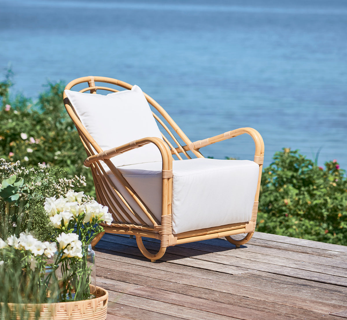 Esta es una imagen de estilo de vida de Charlottenborg sillón lounge exterior en natural Aluminium ArtFibre, en una terraza de madera al aire libre.