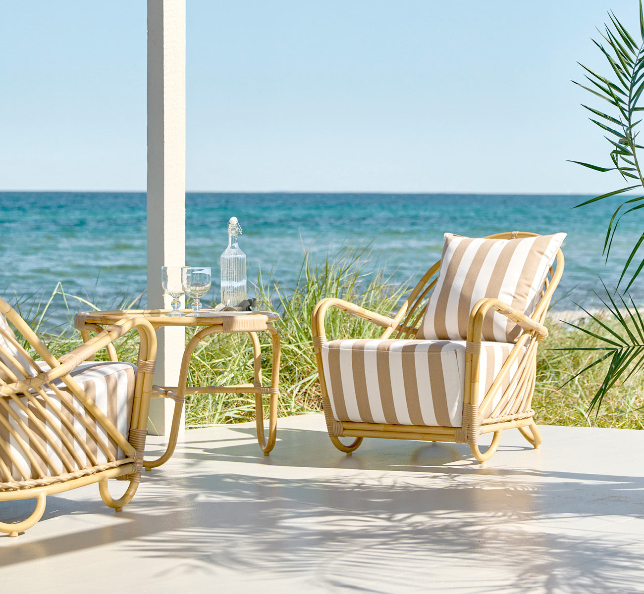 Esta es una imagen de estilo de vida de Charlottenborg sillón lounge exterior en natural Aluminium ArtFibre, en una terraza de madera al aire libre.