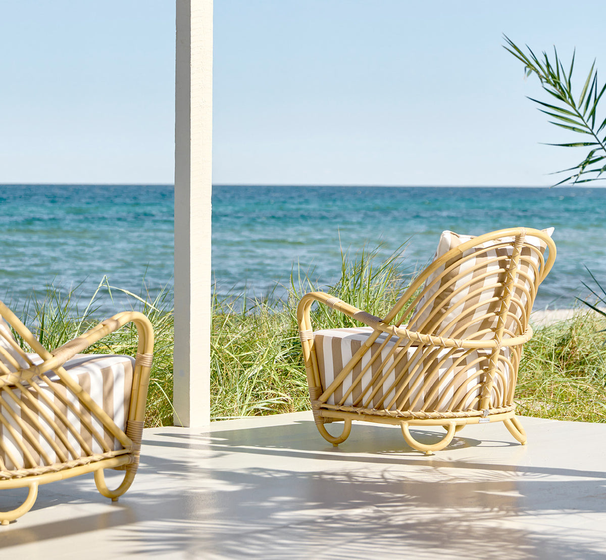 Esta es una imagen de estilo de vida de Charlottenborg sillón lounge exterior en natural Aluminium ArtFibre, en una terraza de madera al aire libre.