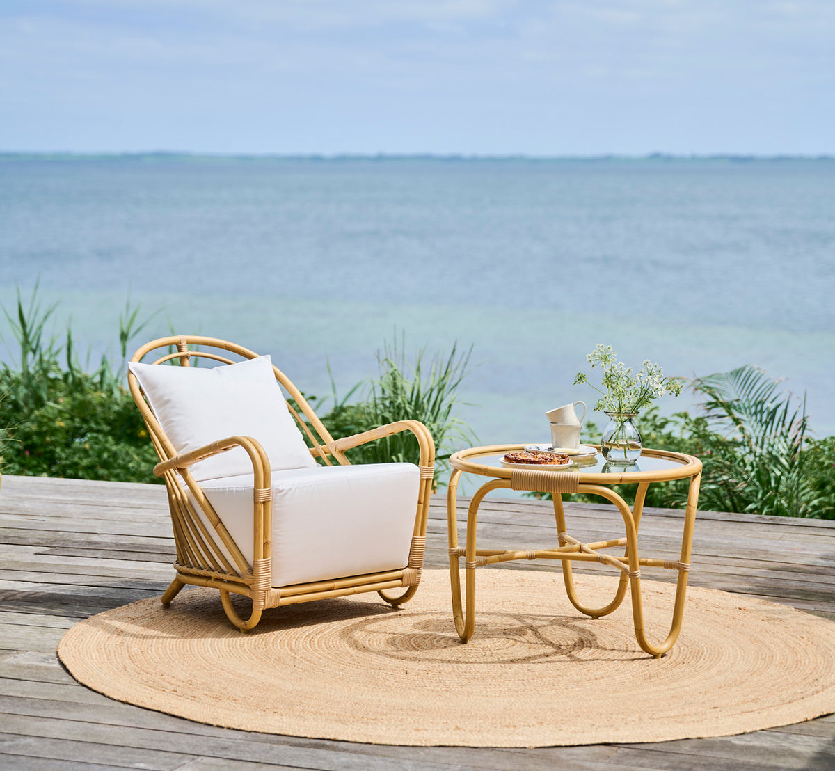 Esta es una imagen de estilo de vida de Charlottenborg sillón lounge exterior en natural Aluminium ArtFibre, en una terraza de madera al aire libre.