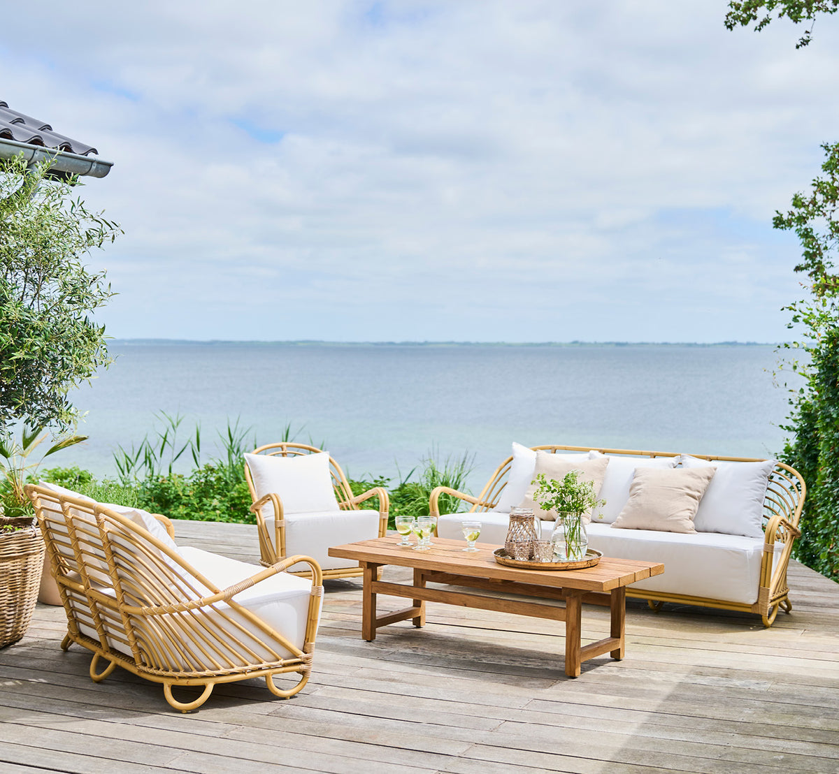 Esta es una imagen de estilo de vida de Charlottenborg sillón lounge exterior en natural Aluminium ArtFibre, en una terraza de madera al aire libre.