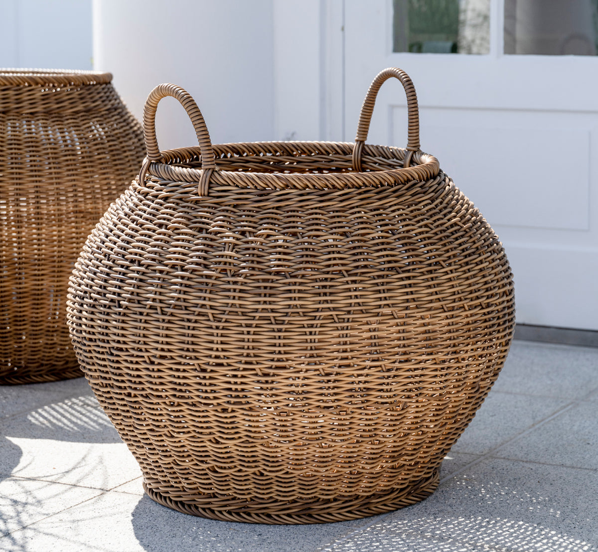 Esta es una imagen de estilo de vida de Smilla cesta en chestnut core weave ArtFibre Aluminium, en un patio exterior soleado con pared blanca y suelo.