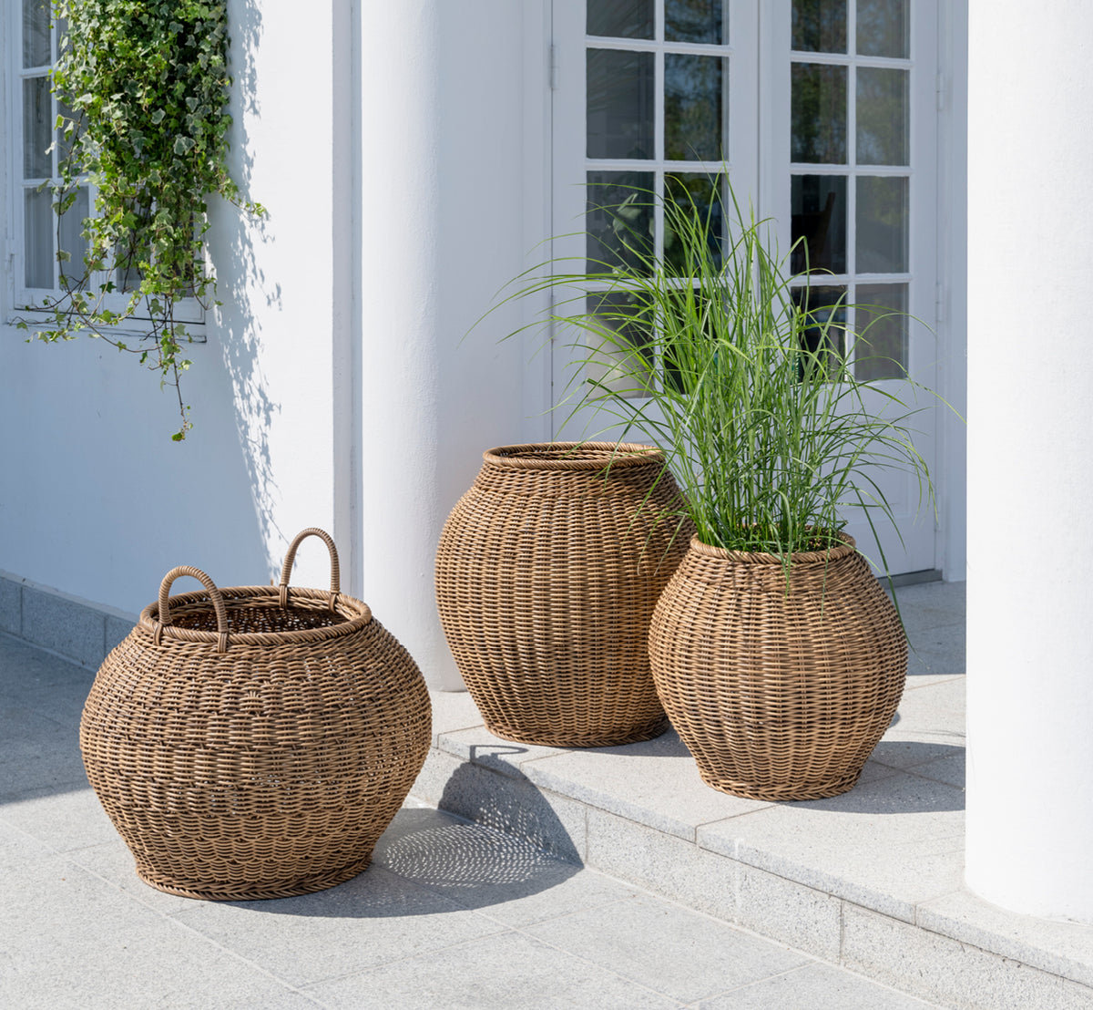 Esta es una imagen de estilo de vida de Smilla cesta en chestnut core weave ArtFibre Aluminium, en un patio exterior soleado con pared blanca y suelo.