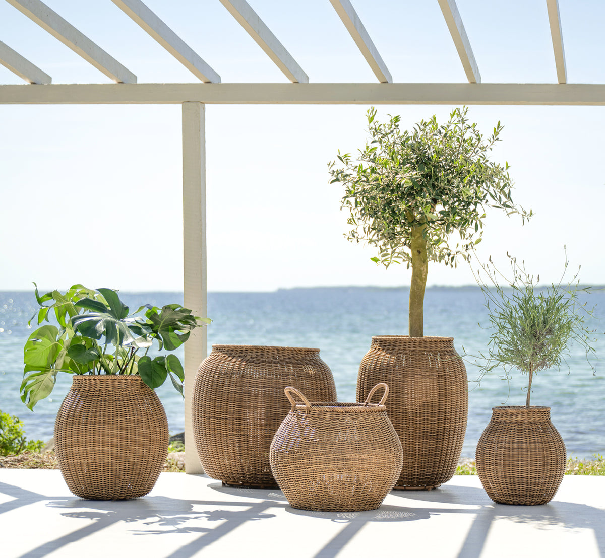 Esta es una imagen de estilo de vida de Ellis cesta en chestnut core weave ArtFibre Aluminium, en un patio exterior soleado con pared blanca y suelo.