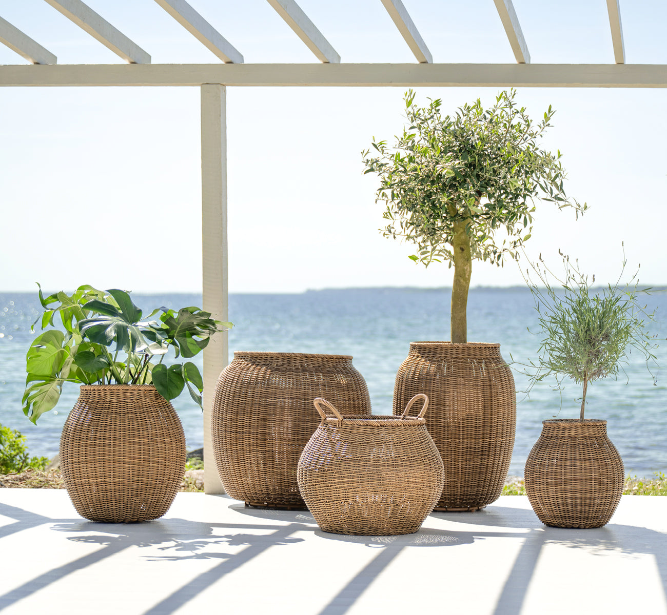 Esta es una imagen de estilo de vida de Ellis cesta en chestnut core weave ArtFibre Aluminium, en un patio exterior soleado con pared blanca y suelo.