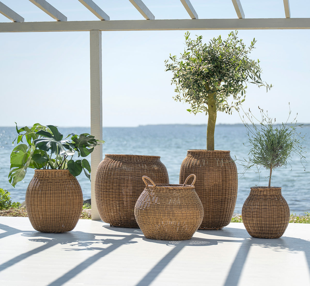 Esta es una imagen de estilo de vida de Alma cesta en chestnut core weave ArtFibre Aluminium, en un patio exterior soleado con pared blanca y suelo.