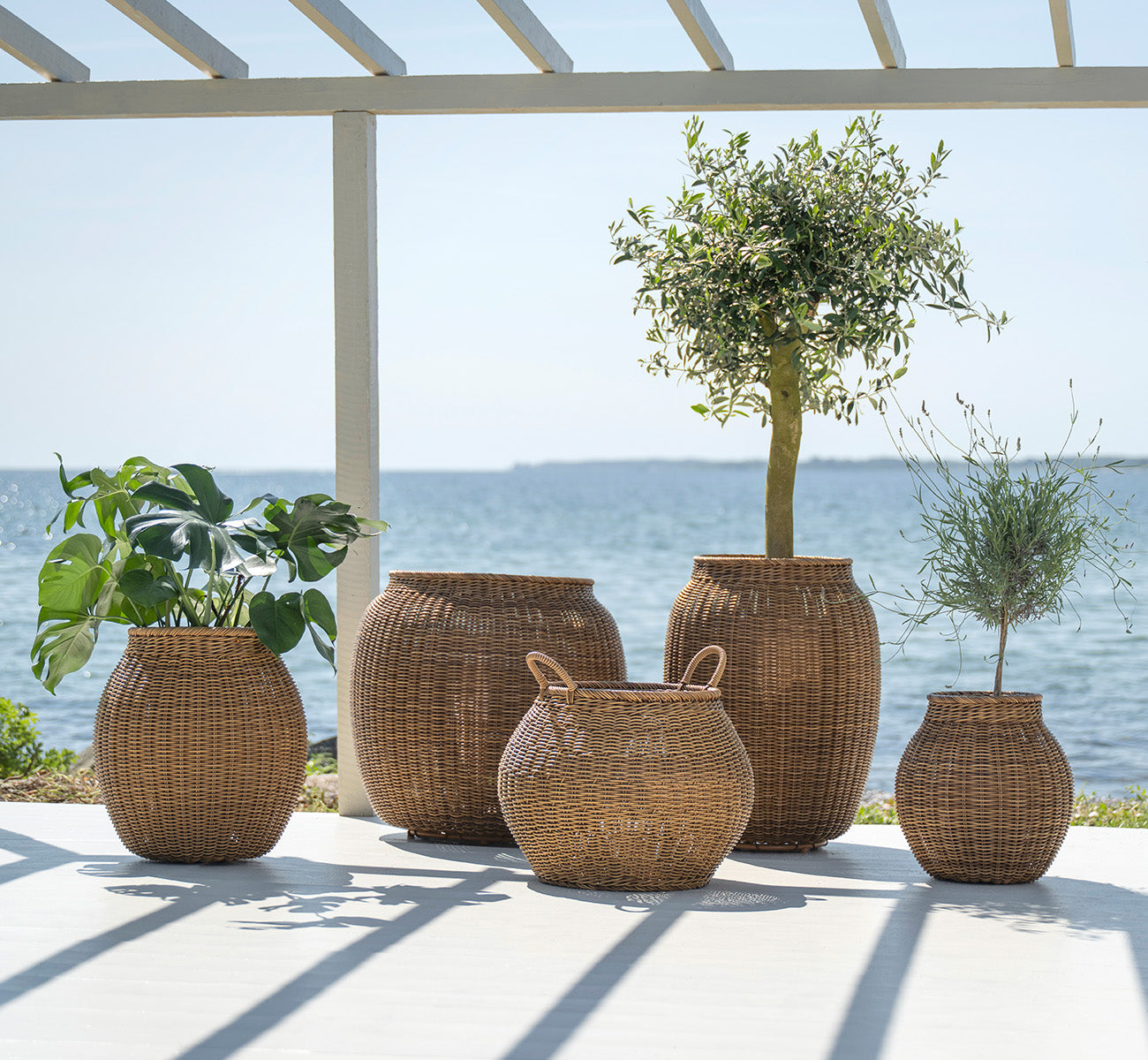 Esta es una imagen de estilo de vida de Alma cesta en chestnut core weave ArtFibre Aluminium, en un patio exterior soleado con pared blanca y suelo.