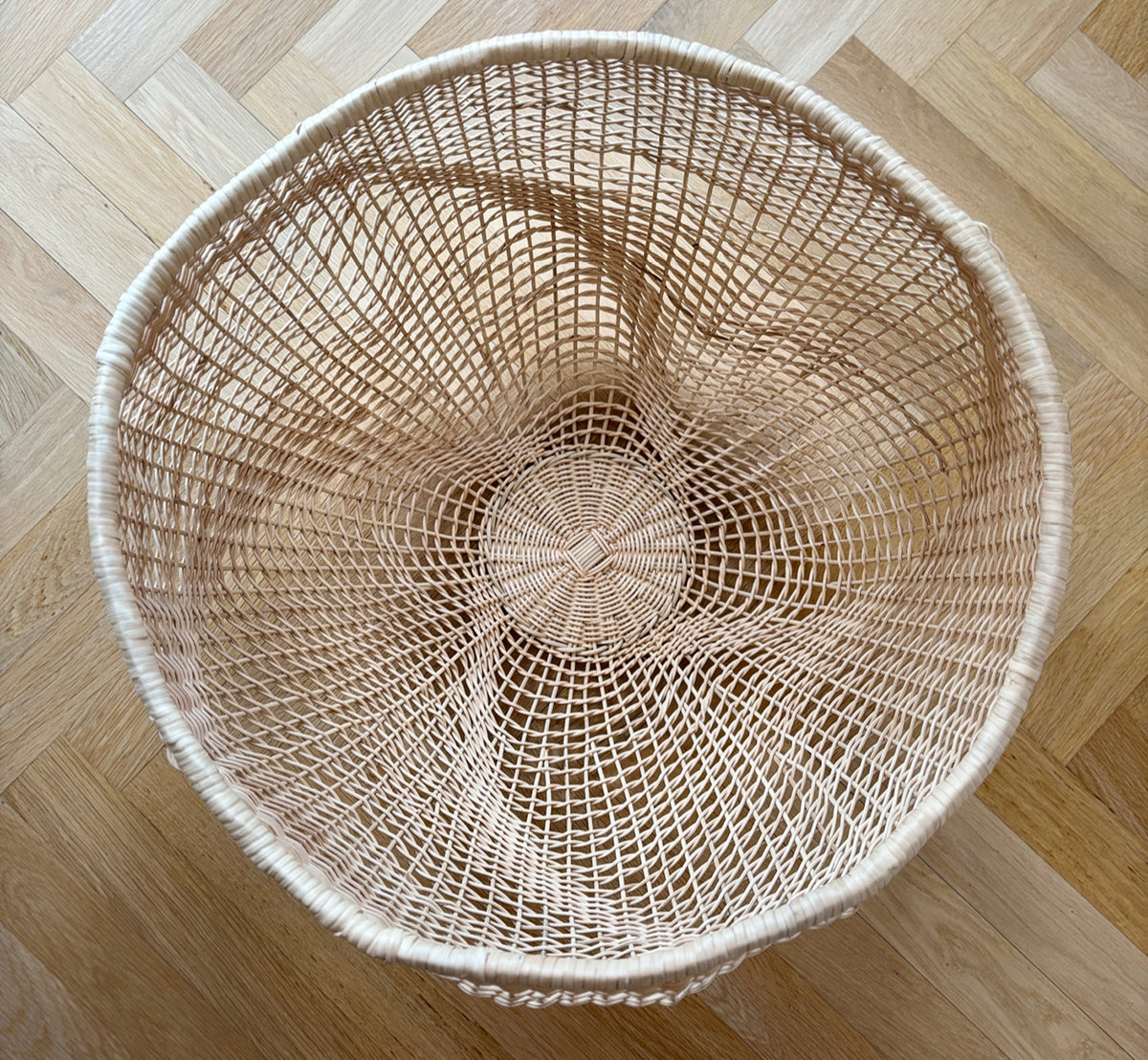 Esta es una imagen de estilo de vida de Folia cesta en natural core weave iron frame, en un interior blanco y luminoso con revestimiento de pared,.