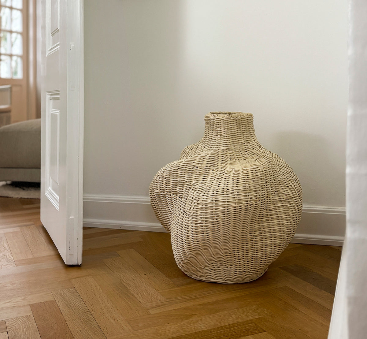 Esta es una imagen de estilo de vida de Solaris Basket Ø40 cm en natural core weave iron frame. Estilizada con flores secas junto a una puerta blanca sobre parqué.