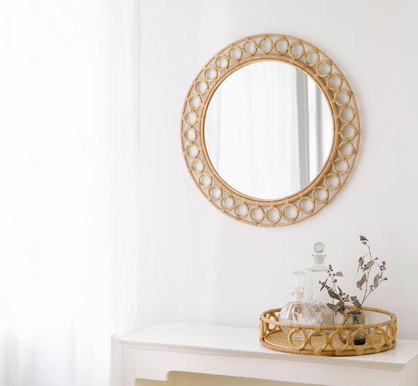Esta es una imagen de estilo de vida de Mira espejo en natural rattan. Montado sobre una consola blanca estilizada con decantadores y ramas secas.