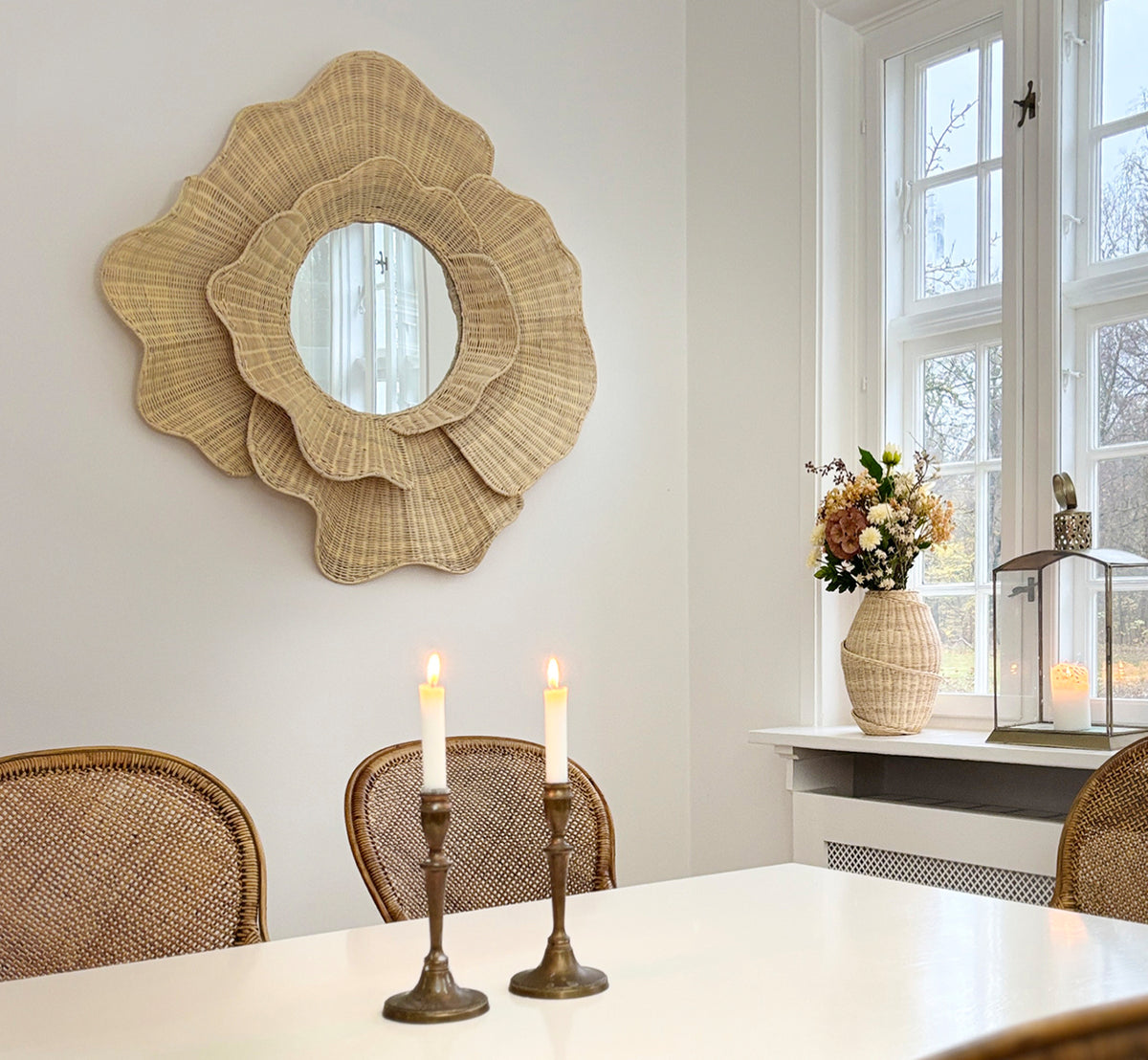 Esta es una imagen de estilo de vida de Floral espejo en natural core weave iron frame, colgado en un luminoso comedor con candelabros y luz natural.