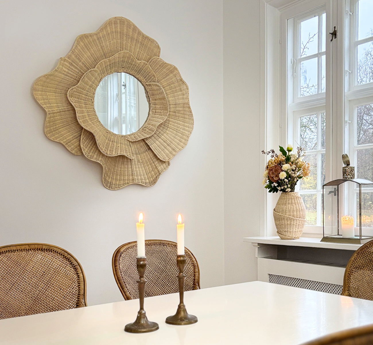Esta es una imagen de estilo de vida de Floral espejo en natural core weave iron frame, colgado en un luminoso comedor con candelabros y luz natural.