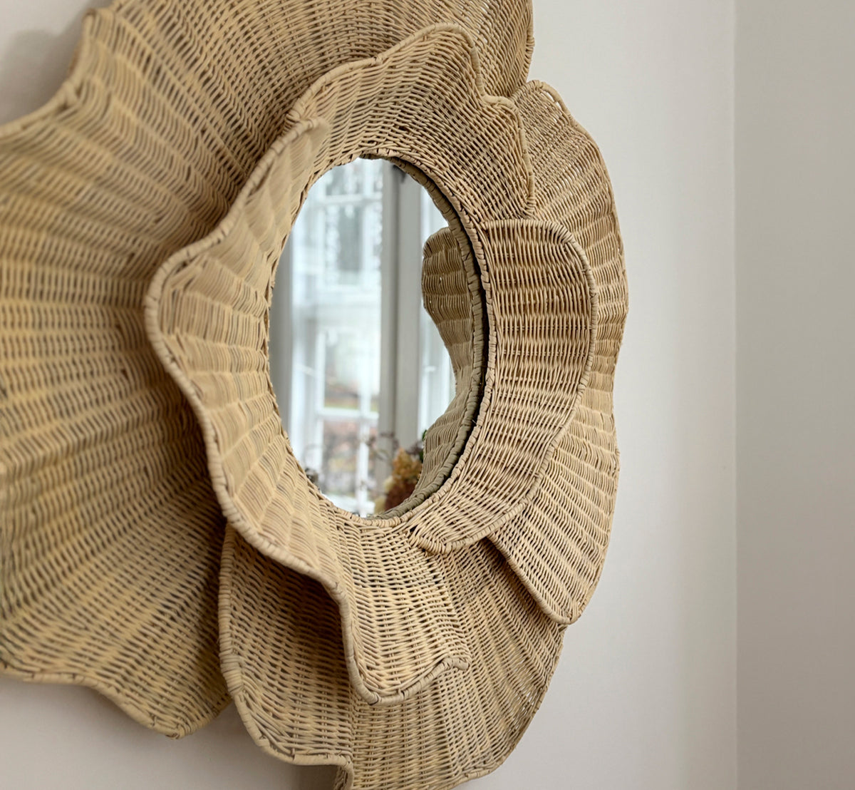 Esta es una imagen de estilo de vida de Floral espejo en natural core weave iron frame, colgado en un luminoso comedor con candelabros y luz natural.
