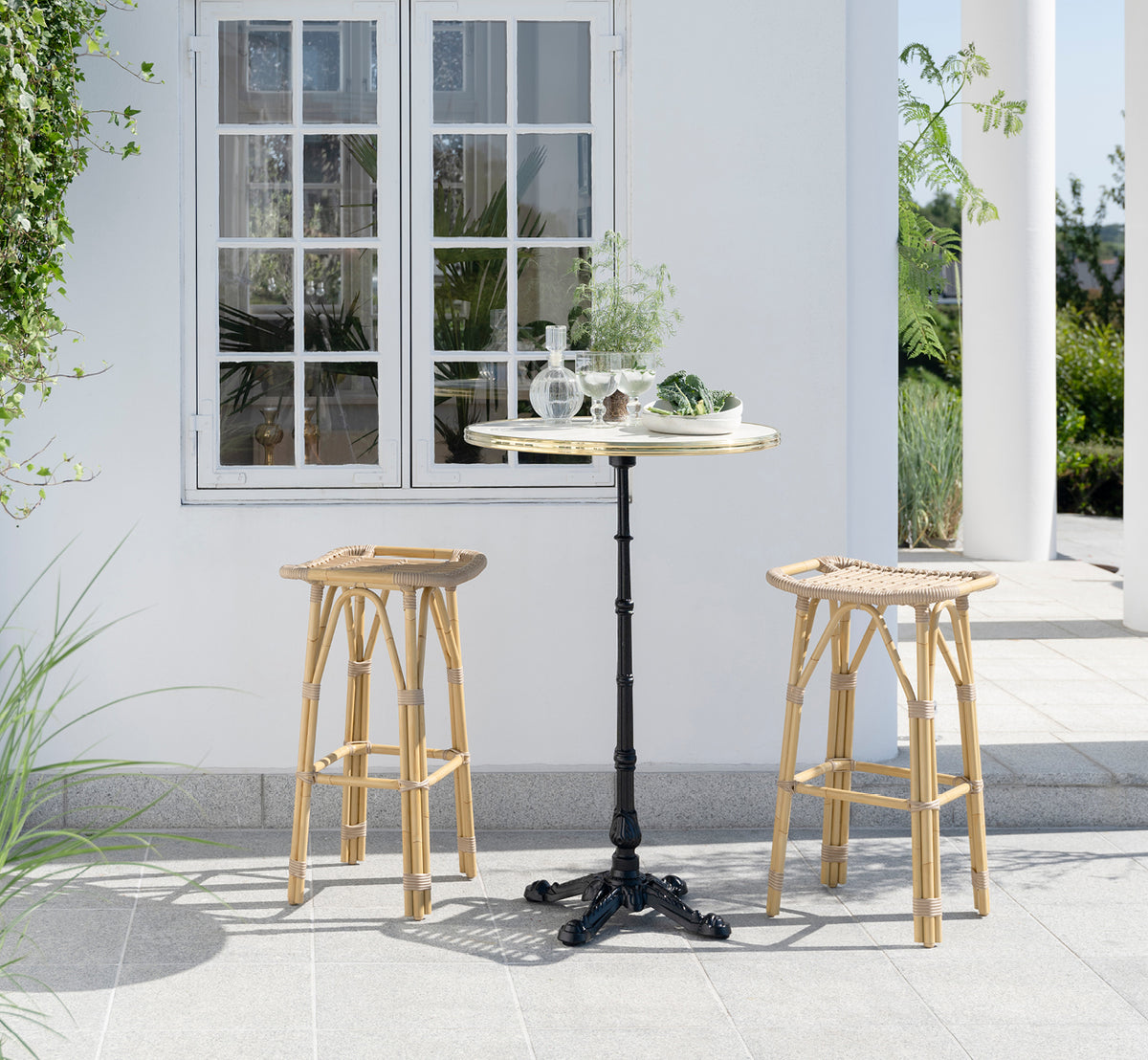 Esta es una imagen de estilo de vida de Lyon mesa de bar Versalite Marble Ø70 cm en cast iron. Elegante patio con taburetes de bar y plantas verdes.