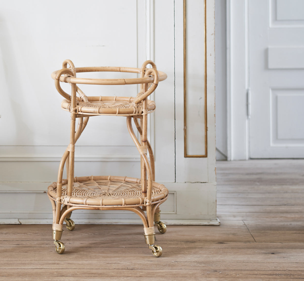 Esta es una imagen de estilo de vida de Fratellino carrito en polished Natural Rattan, en un interior clásico con elaboradas puertas de paneles.