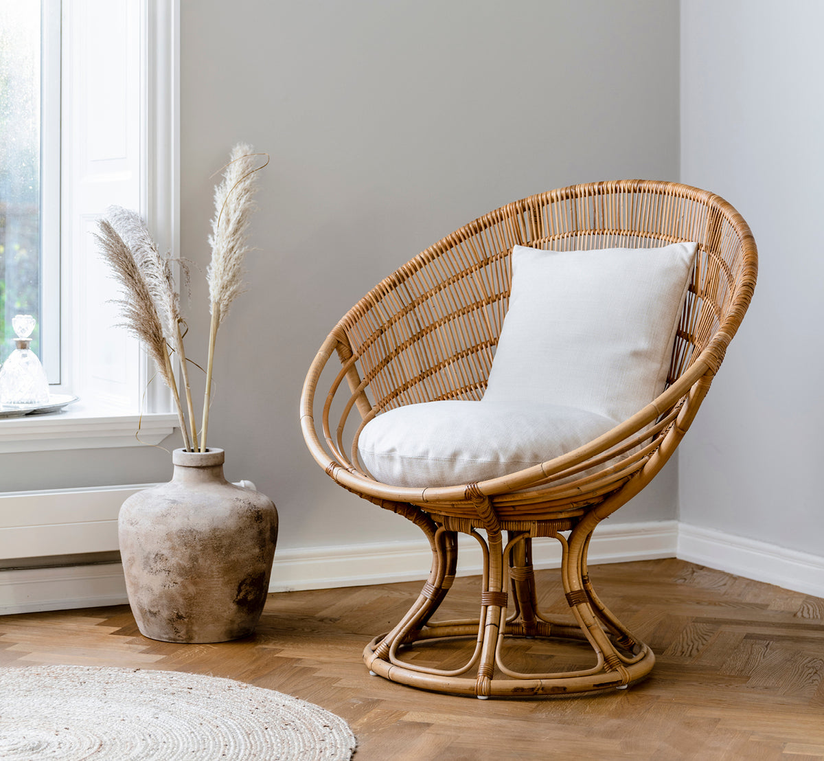 Esta es una imagen de estilo de vida de Luna sillón lounge en natural skin on rattan. Estilizada con un cojín blanco en un rincón acogedor con decoración de hierba de las pampas.