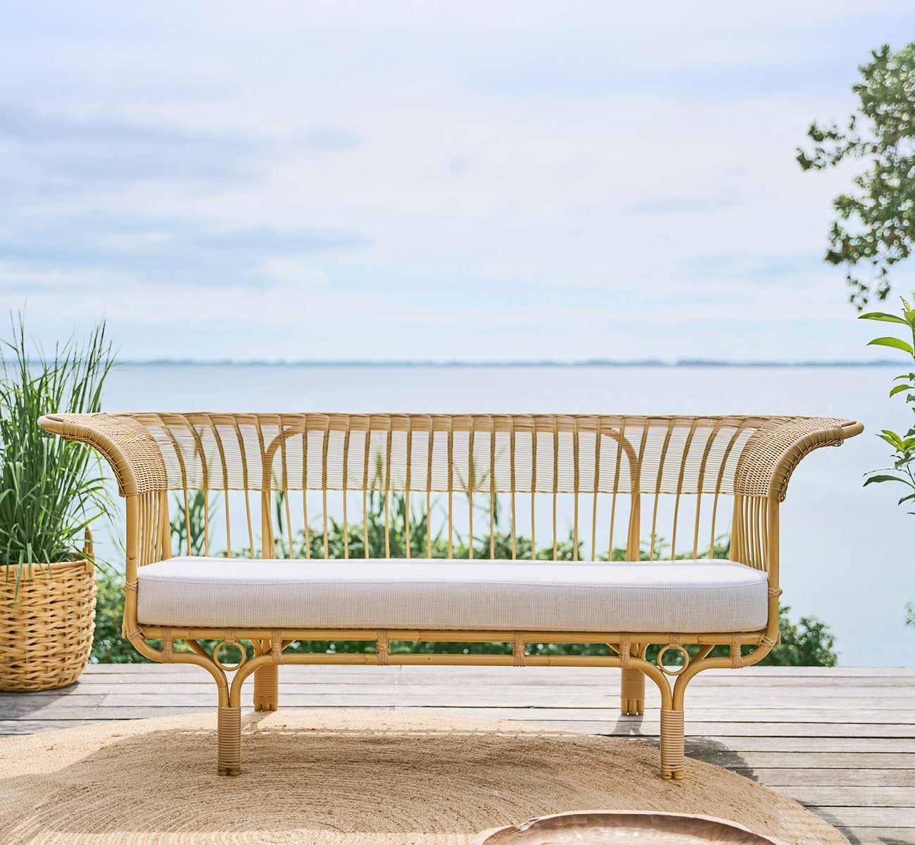 Esta es una imagen de estilo de vida de Belladonna sofá exterior en natural Aluminium ArtFibre, en una terraza de madera al aire libre con vistas al.
