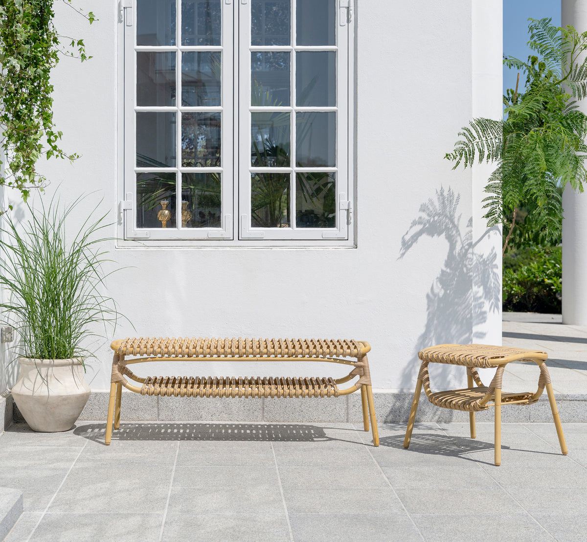 Esta es una imagen de estilo de vida de Machiya taburete exterior en natural aluminium artfibre. Patio blanco con banco exterior y plantas verdes.