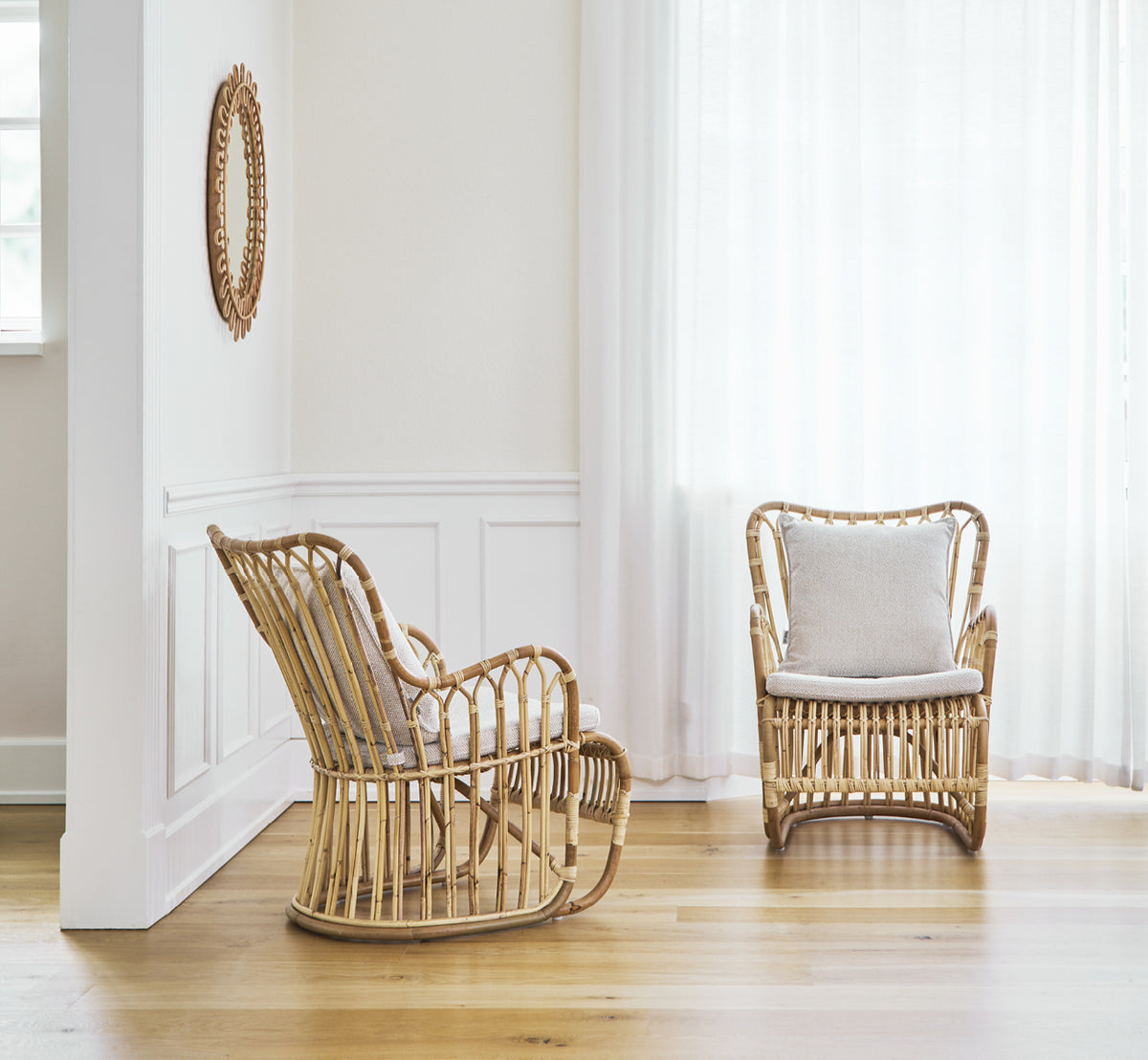 Esta es una imagen de estilo de vida de Tulip sillón lounge en polished natural rattan. Combinada con un sofá a juego en una sala luminosa con paneles y puerta.