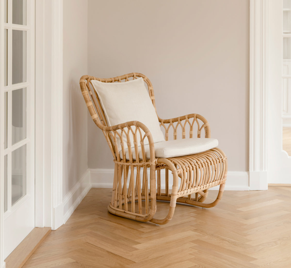 Esta es una imagen de estilo de vida de Tulip sillón lounge en polished natural rattan. Combinada con un sofá a juego en una sala luminosa con paneles y puerta.