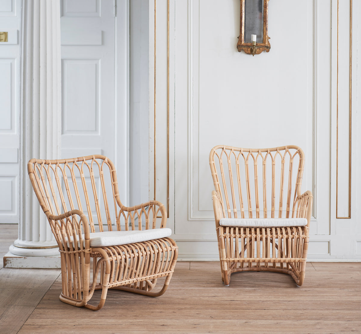 Esta es una imagen de estilo de vida de Tulip sillón lounge en polished natural rattan. Combinada con un sofá a juego en una sala luminosa con paneles y puerta.
