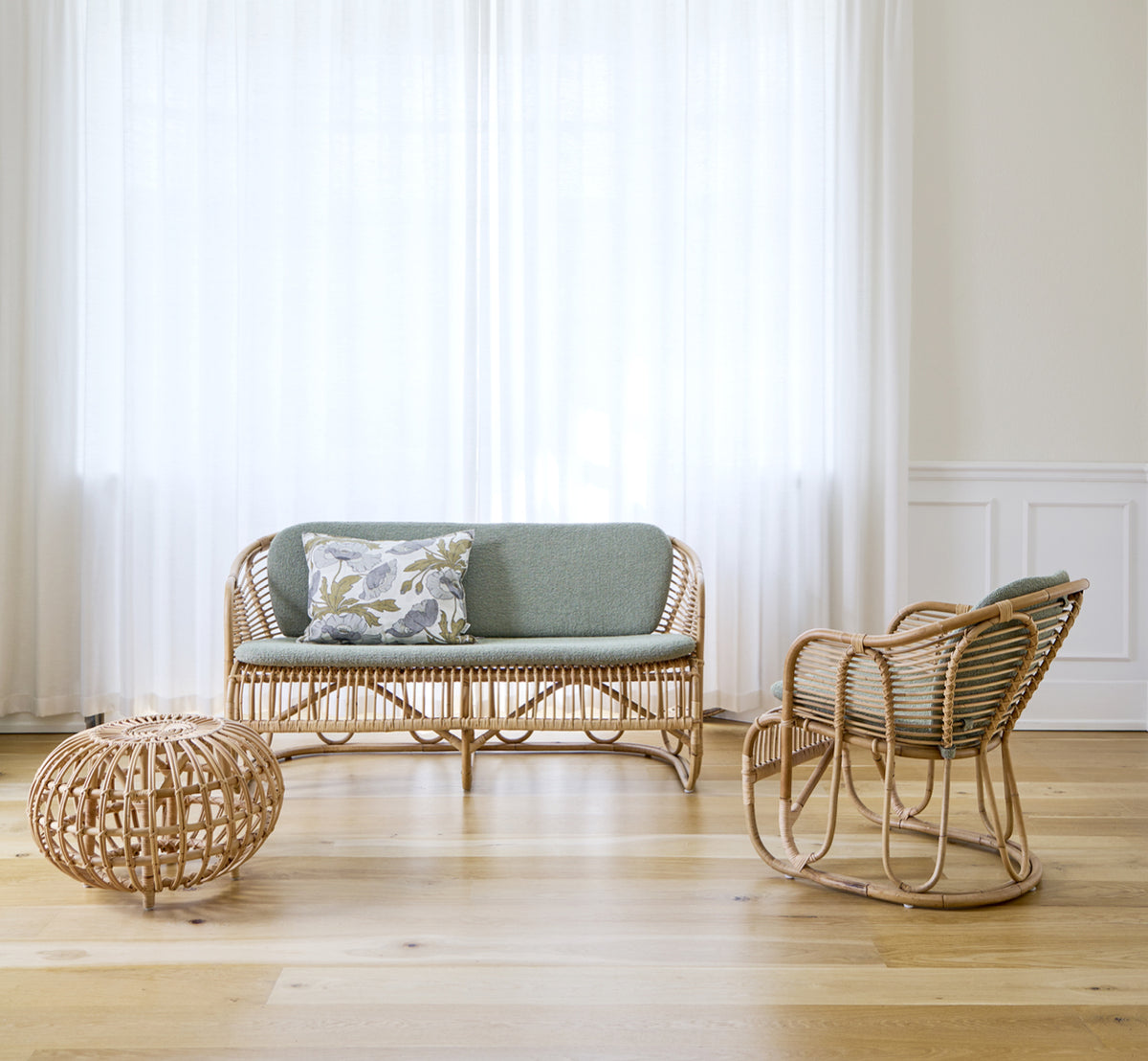 Esta es una imagen de estilo de vida de Swing sillón lounge en polished natural rattan. De pie sola junto a una planta frondosa en un suelo de parqué en espiga.