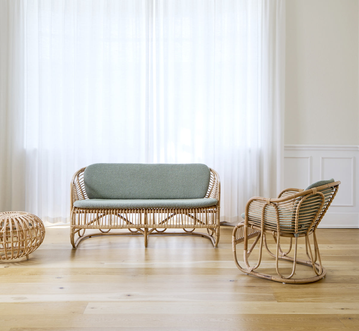 Esta es una imagen de estilo de vida de Swing sofá en polished natural rattan. Colocado sobre una alfombra junto a una planta ficus lyrata en suelo de parqué.