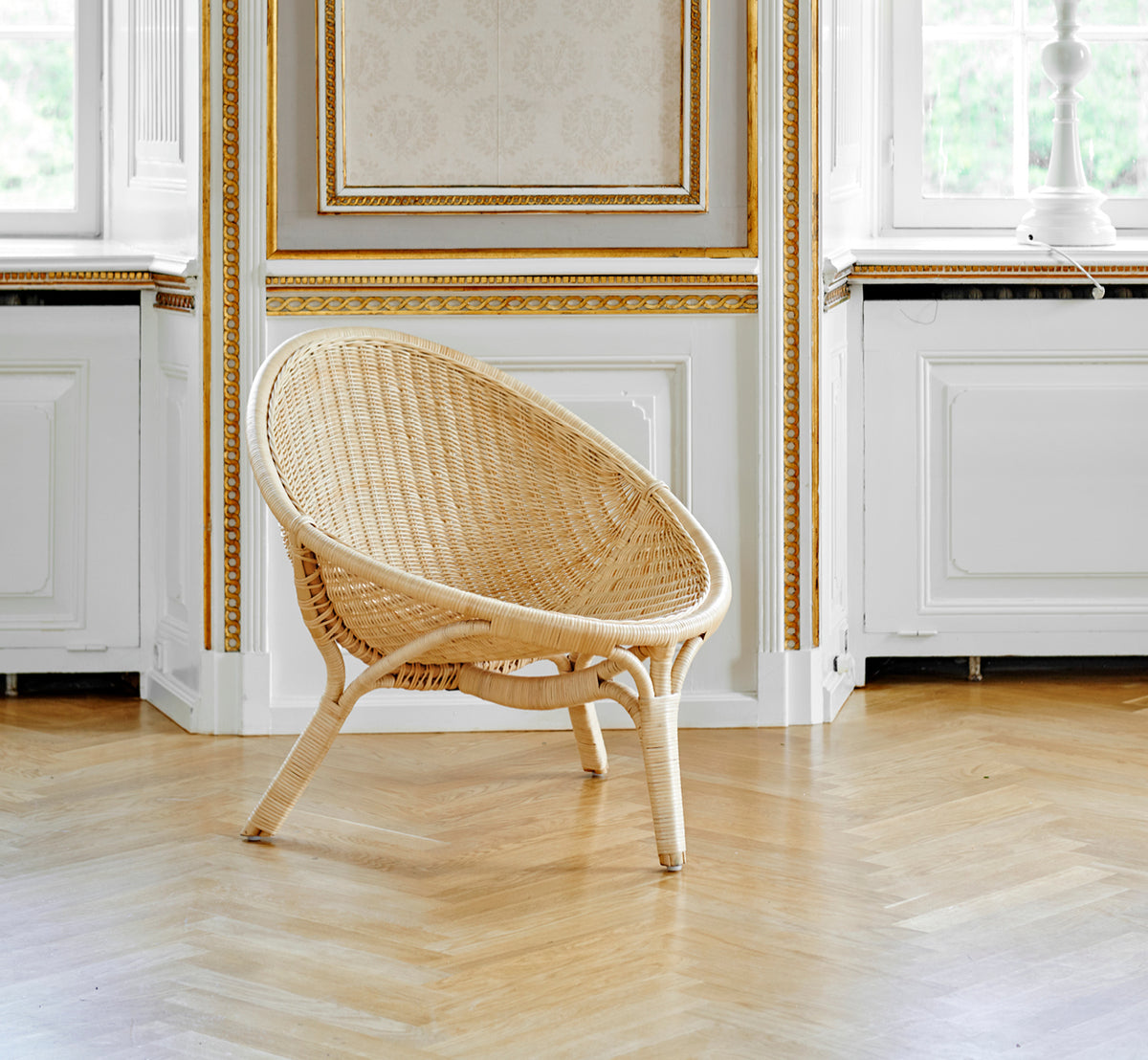 Esta es una imagen de estilo de vida de Rana sillón lounge en natural core weave rattan frame. De pie sola en una sala con paneles dorados y suelo de parqué.