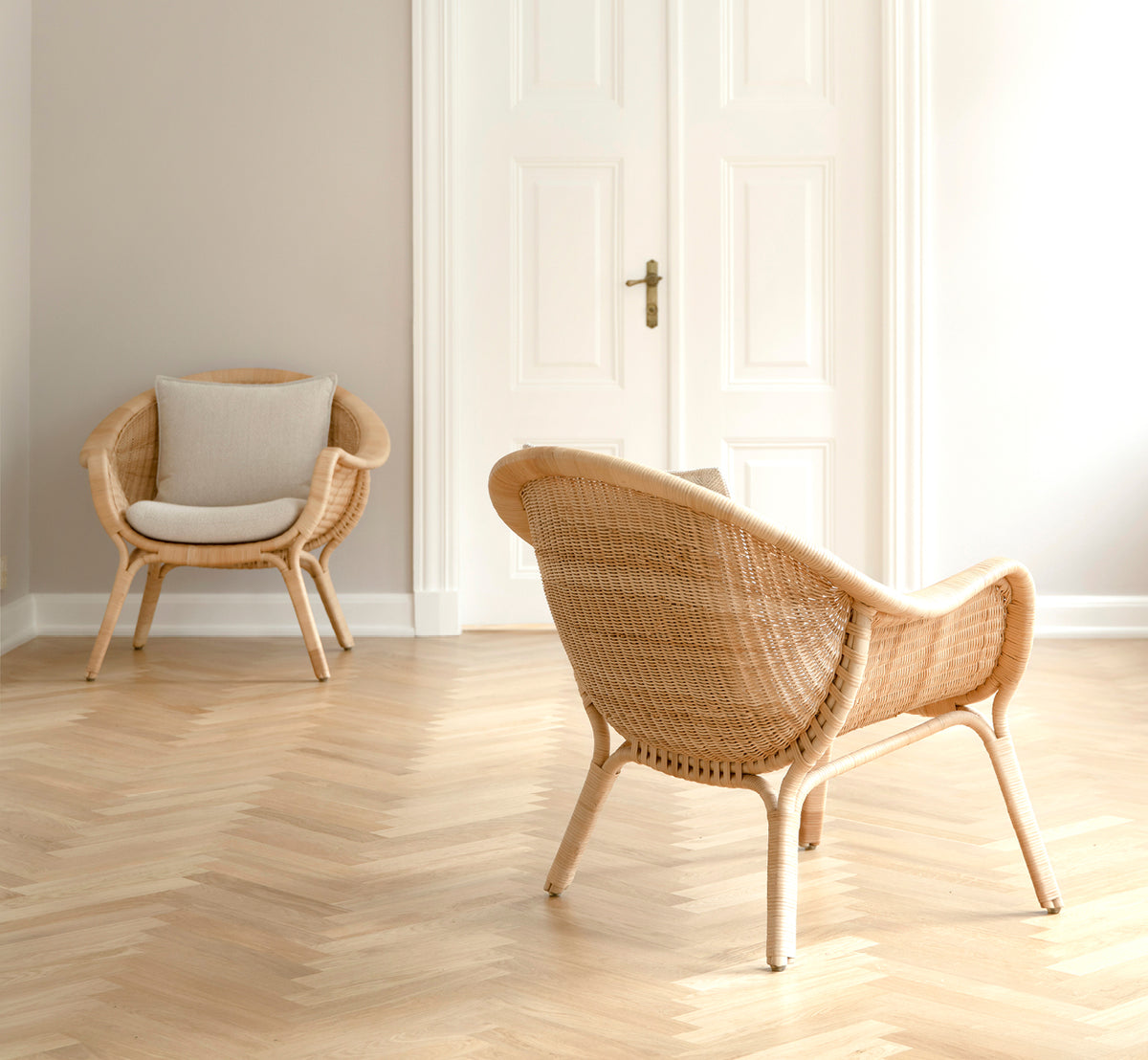 Esta es una imagen de estilo de vida de Madame sillón lounge en natural core weave rattan frame. Sala luminosa con suelo en espiga y puertas dobles blancas.