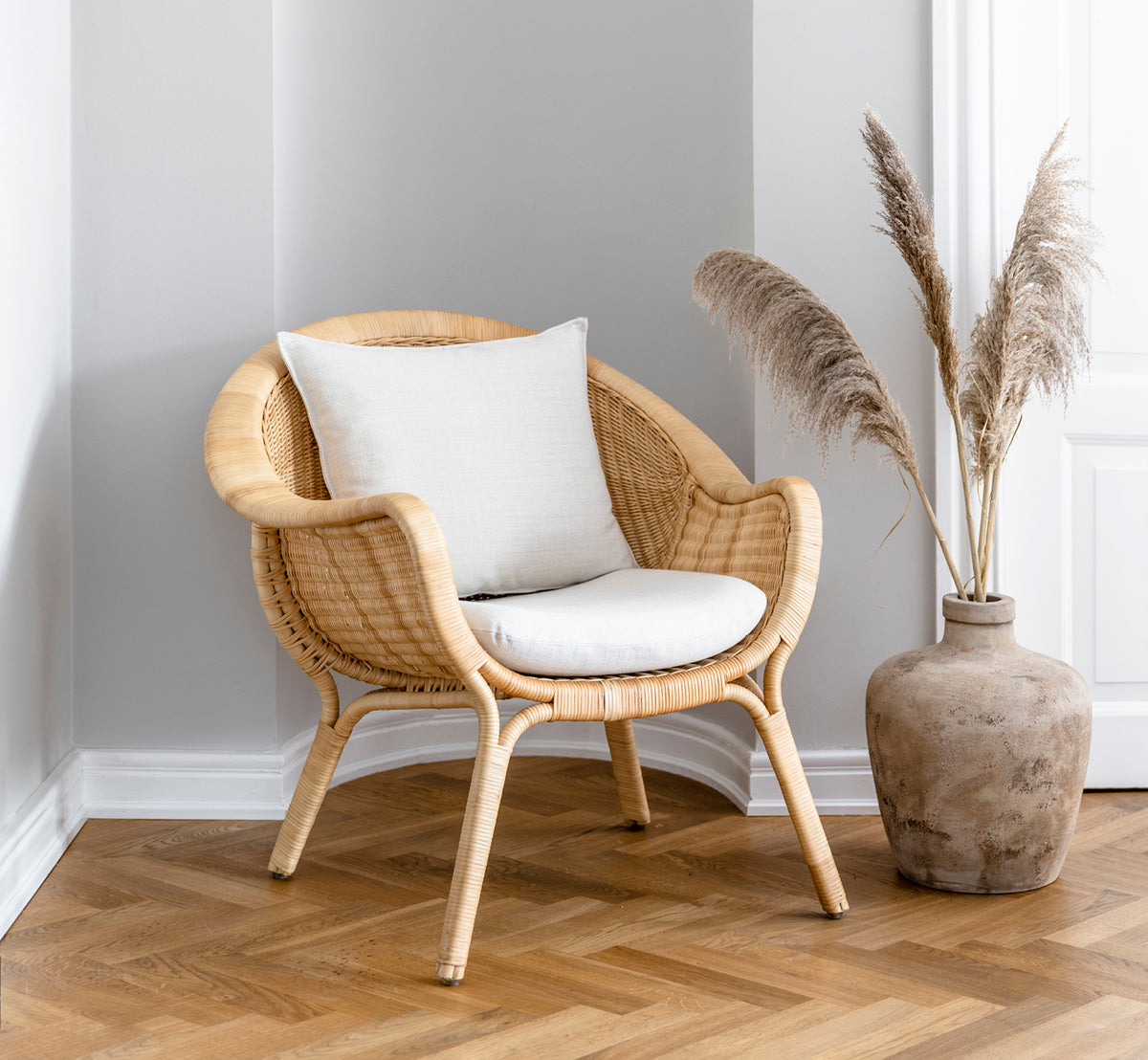 Esta es una imagen de estilo de vida de Madame sillón lounge en natural core weave rattan frame. Rincón acogedor con suelo en espiga y jarrón con hierba de las pampas.