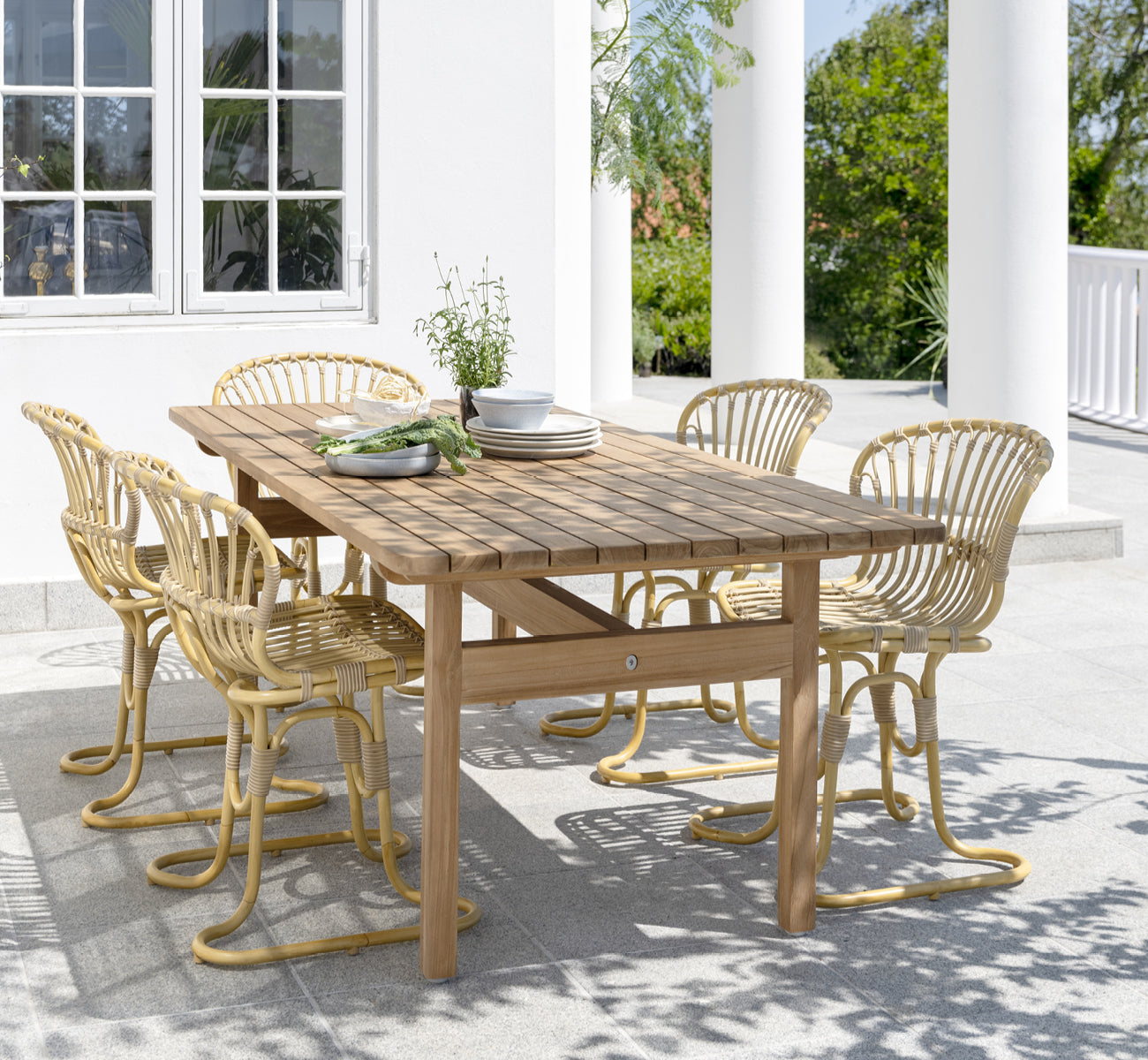 Esta es una imagen de estilo de vida de Rita silla de comedor exterior en natural aluminium artfibre. Combinado con una mesa bistró en una terraza blanca con columnas.