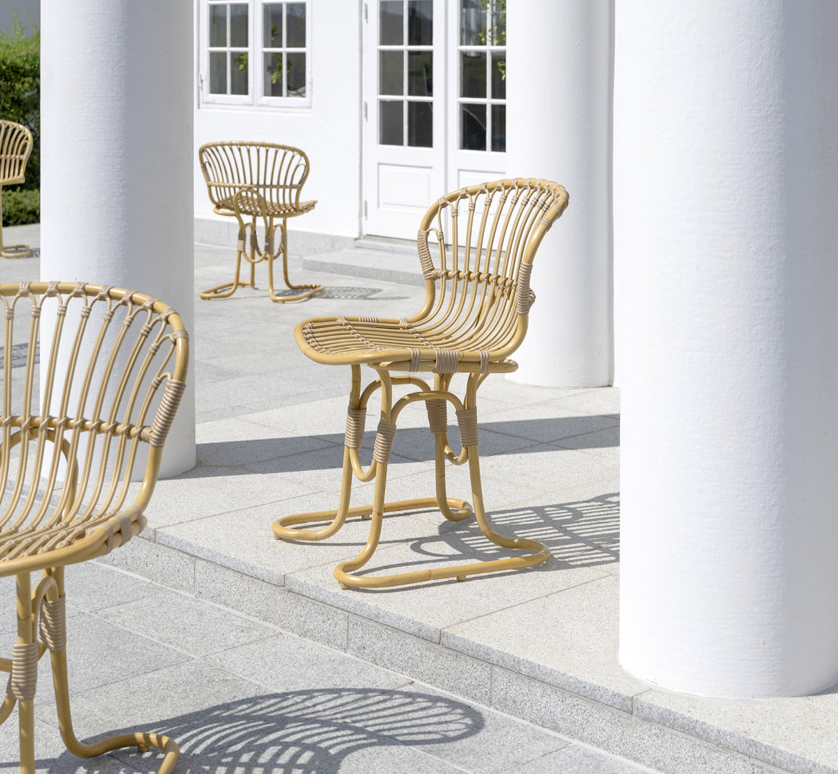 Esta es una imagen de estilo de vida de Rita silla de comedor exterior en natural aluminium artfibre. Combinado con una mesa bistró en una terraza blanca con columnas.